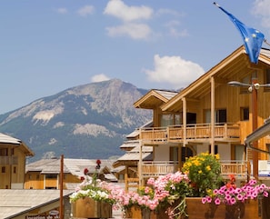 Eine Holzhütte mit Balkon, umgeben von Blumenkästen vor einer Bergkulisse.