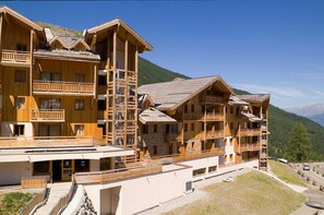 Un chalet en bois à plusieurs étages, doté de balcons, qui se dresse sur un fond de paysage montagneux.