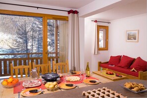 Un coin repas avec une table en bois dressée pour le repas, un canapé avec des coussins rouges et une fenêtre avec des rideaux.