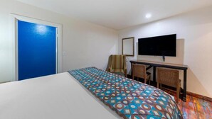 Hotellihuone, jossa on sänky, työpöytä ja kaksi tuolia, televisio ja sininen ovi.