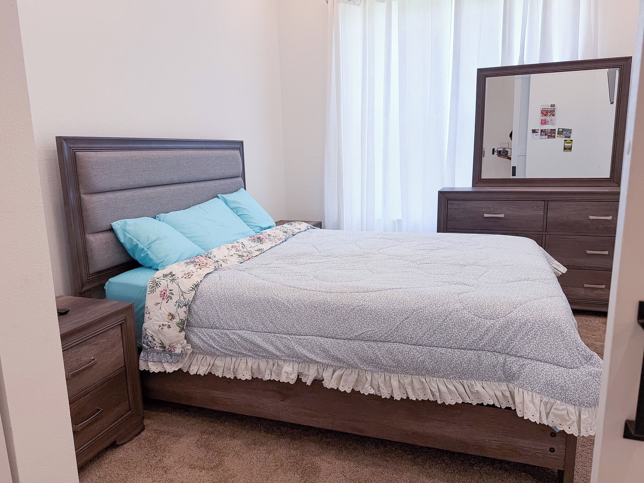A bedroom with a bed, a nightstand, a dresser, and a mirror.