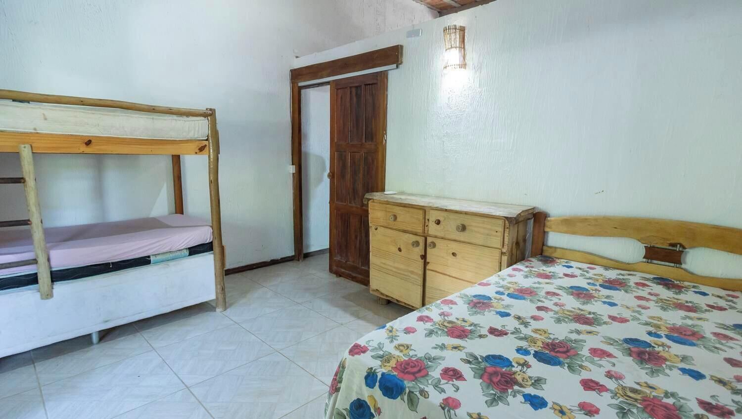 Een slaapkamer met een stapelbed, een houten dressoir en een bed met een bloemenbedekking.