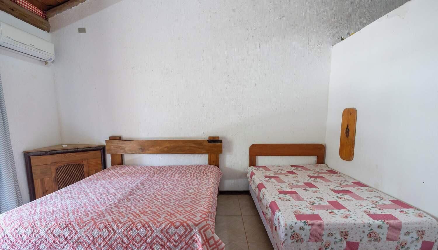 A room with two beds, a wooden headboard, a small wooden dresser, and a wall-mounted light fixture.