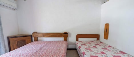 Una habitación con dos camas, un cabecero de madera, un pequeño aparador de madera y una lámpara de pared.