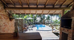 A wooden deck with a pool, outdoor seating, and a brick oven.