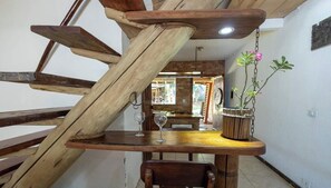 Una escalera espiral de madera con una mesa en la parte inferior, una planta en maceta y una copa de vino.