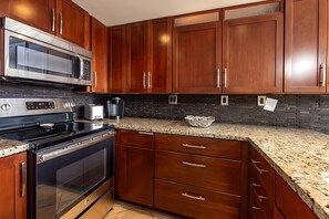 A kitchen with wooden cabinets, a stainless steel microwave, a toaster, and a coffee maker. - Bright 4BR, 2 Condos for 12 at Maalaea Kai! (Wailuku)