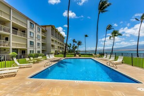 A swimming pool with lounge chairs, a building with balconies, and palm trees. - Bright 4BR, 2 Condos for 12 at Maalaea Kai! (Wailuku)