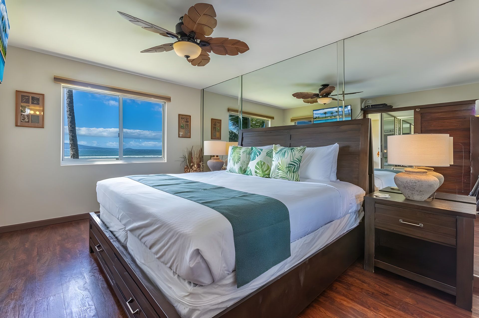 A hotel room with a large bed, a ceiling fan, a window with a view, a mirror, and a nightstand.