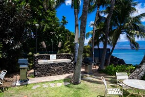 A patio area with a stone wall, outdoor seating, and a view of the ocean. - Bright 4BR, 2 Condos for 12 at Maalaea Kai! (Wailuku)