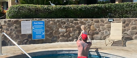 A swimming pool with a stone wall, a lifeguard tower, and a sign indicating pool rules.