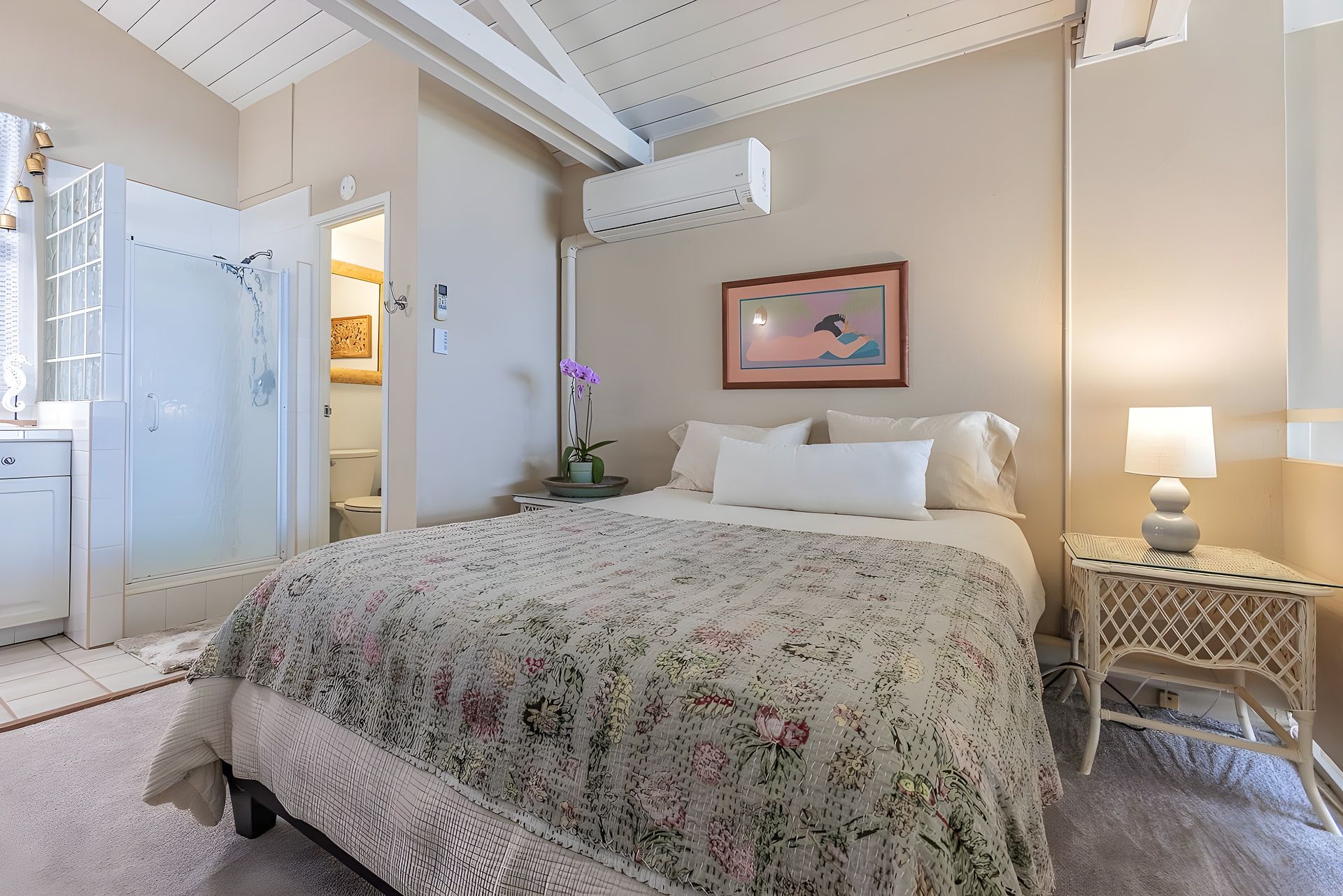 A bedroom with a bed, bedside table, lamp, and a painting on the wall.