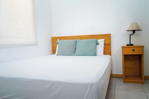 A single bed with a wooden headboard, a bedside table with a lamp, and a window with blinds. - 4-Bedroom Private Beach House with AC and access to the beach at 3-min walk (La Libertad)