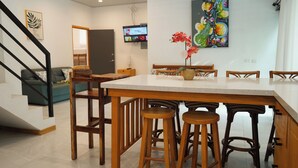 A modern kitchen with a wooden table, bar stools, and a TV mounted on the wall. - 4-Bedroom Private Beach House with AC and access to the beach at 3-min walk (La Libertad)