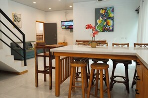 A modern kitchen with a wooden table, bar stools, and a TV mounted on the wall. - 4-Bedroom Private Beach House with AC and access to the beach at 3-min walk (La Libertad)