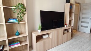 A living room with a flat-screen TV, wooden shelves, and a potted plant. - Blue Dream - Warsaw Ochota Apartment - Easy Access to Chopin Airport (Warszawa)