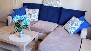 A modern living room with a sectional sofa, a coffee table, and a vase with flowers. - Blue Dream - Warsaw Ochota Apartment - Easy Access to Chopin Airport (Warszawa)