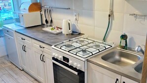 Moderni keittiö, jossa on valkoiset kaapit, kaasuliesi, pesuallas ja ikkuna, josta on näkymä rakennuksiin.