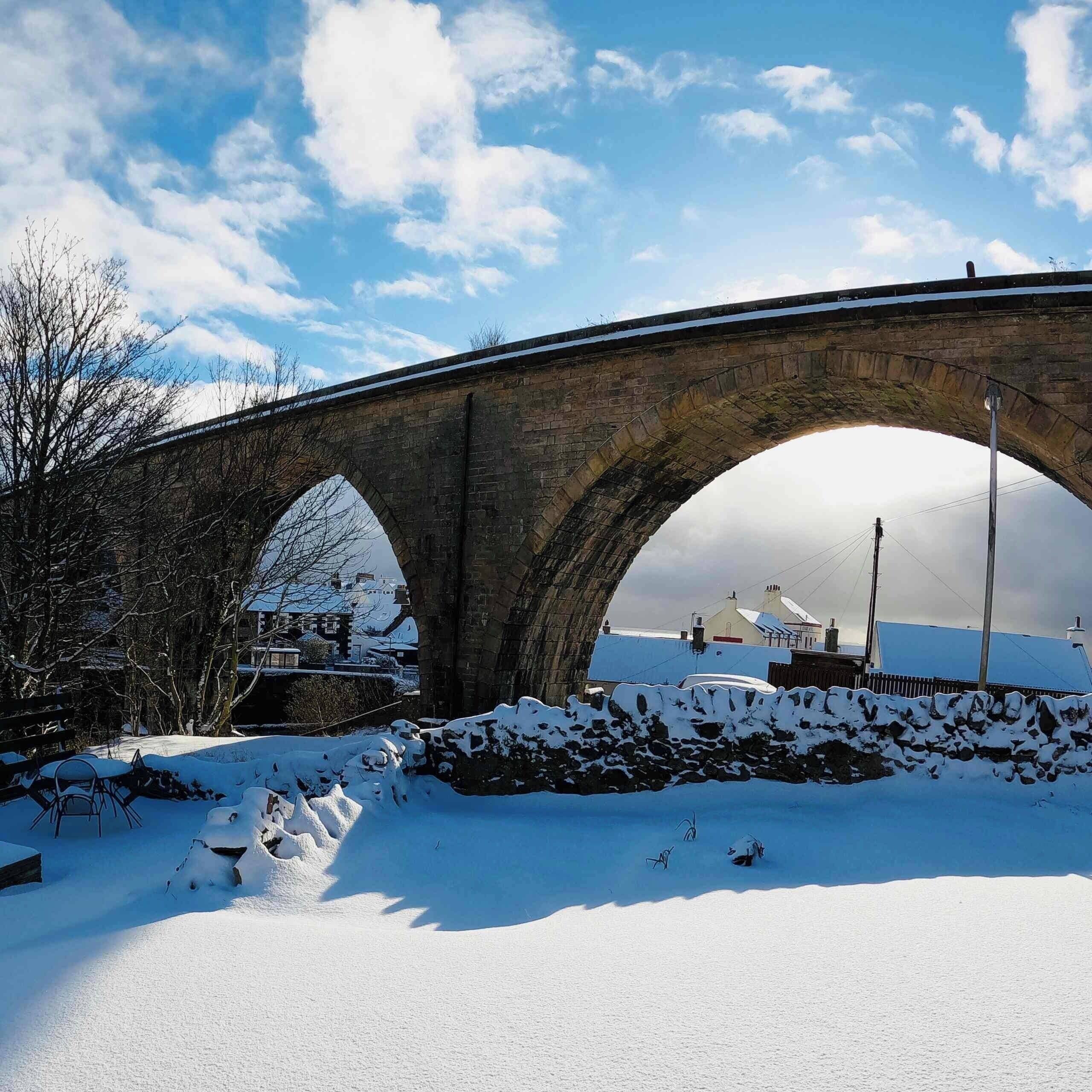 Eine Steinbrücke mit drei Bögen, umgeben von schneebedecktem Boden und Bäumen.