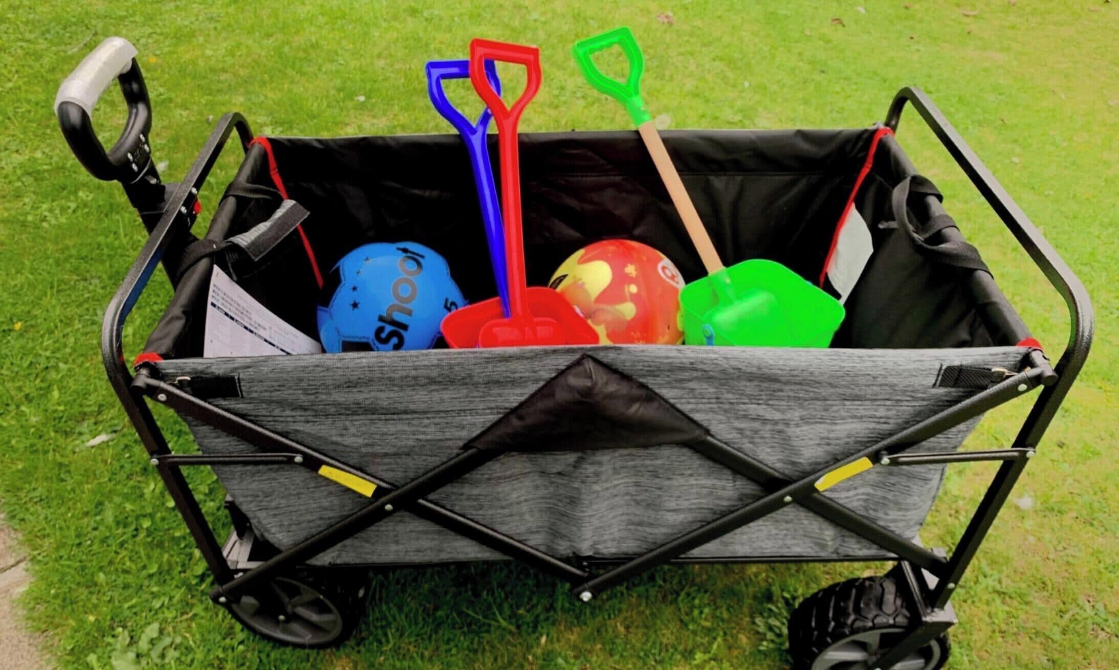 A black wheeled cart with a black interior, containing colorful plastic shovels and a blue ball with 'shoot' written on it.