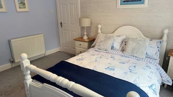 A bedroom with a white bed, a nightstand, a lamp, and a framed picture on the wall.