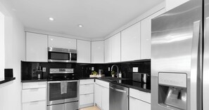 A modern kitchen with stainless steel appliances, white cabinetry, and black countertops. - Comfort 2BR - Private Balcony & Beach access (Sunny Isles Beach)