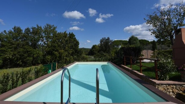 A rectangular swimming pool with a clear blue water surface, surrounded by a stone wall and metal railings, set against a backdrop of trees and a clear sky. - Sant'Ignazio Farm (Toscana)