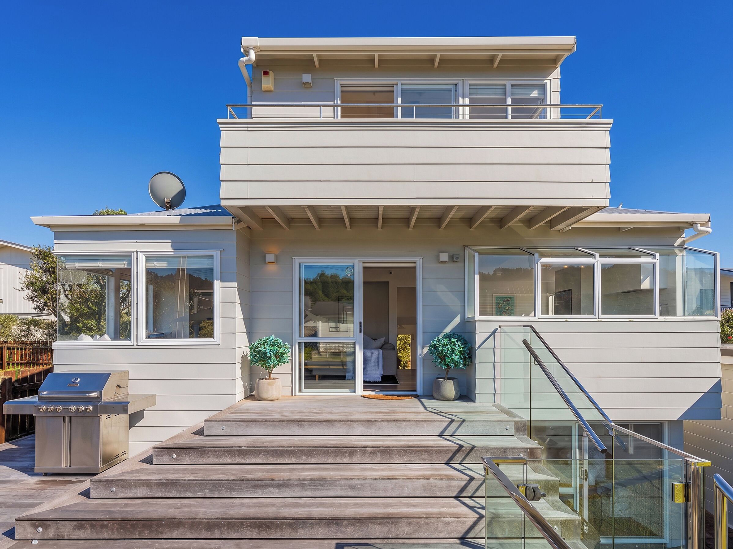 A two-story house with a covered patio, a grill, and a staircase leading to the entrance.