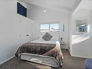 A bedroom with a bed, a window, a wardrobe, and a bedside table. - Sandy Strides - Whangamata Holiday Home (Whangamata)