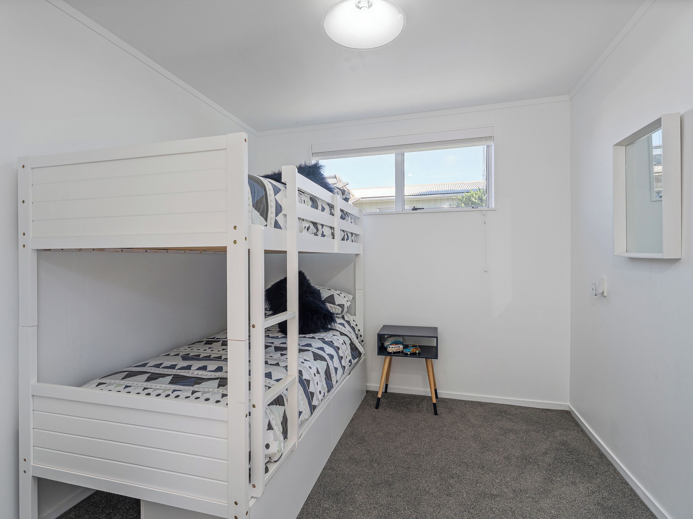 A bunk bed room with a small table and a window.