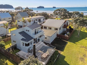 A residential area with houses, a grassy yard, and a view of the ocean. - Sandy Strides - Whangamata Holiday Home (Whangamata)
