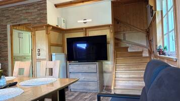 Un salon confortable avec un escalier en bois, un téléviseur à écran plat et une table à manger avec des chaises.