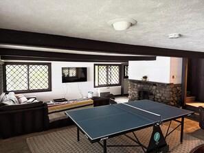 A living room with a ping pong table, a sofa, a TV, and a stone fireplace.