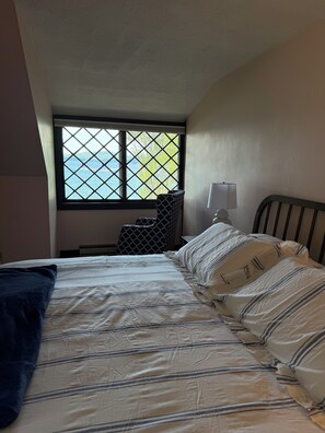 A bedroom with a bed, a nightstand, a lamp, and a window with a view of the sea.