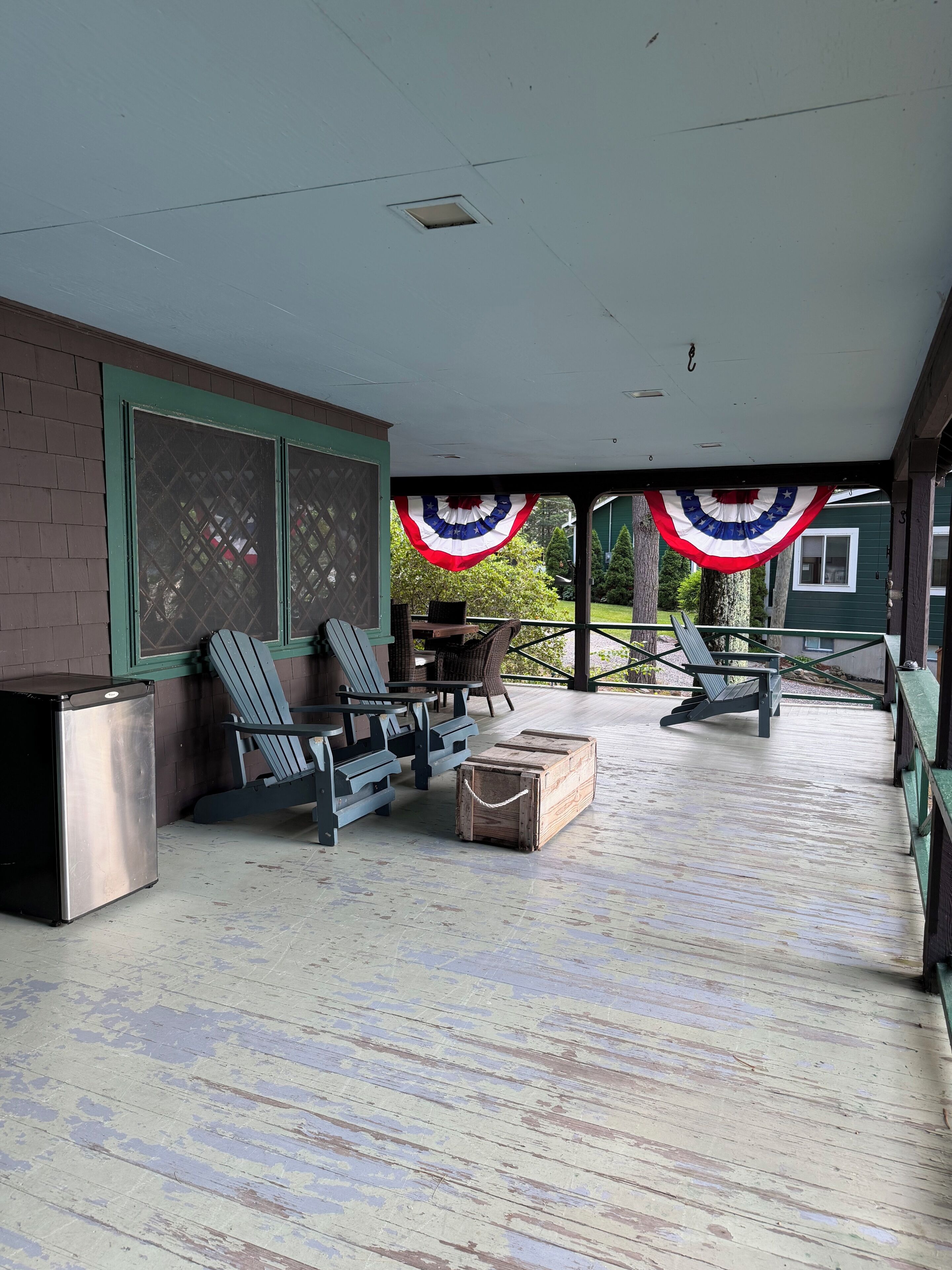 A covered outdoor seating area with chairs and a table, a small refrigerator, and a decorative American flag.