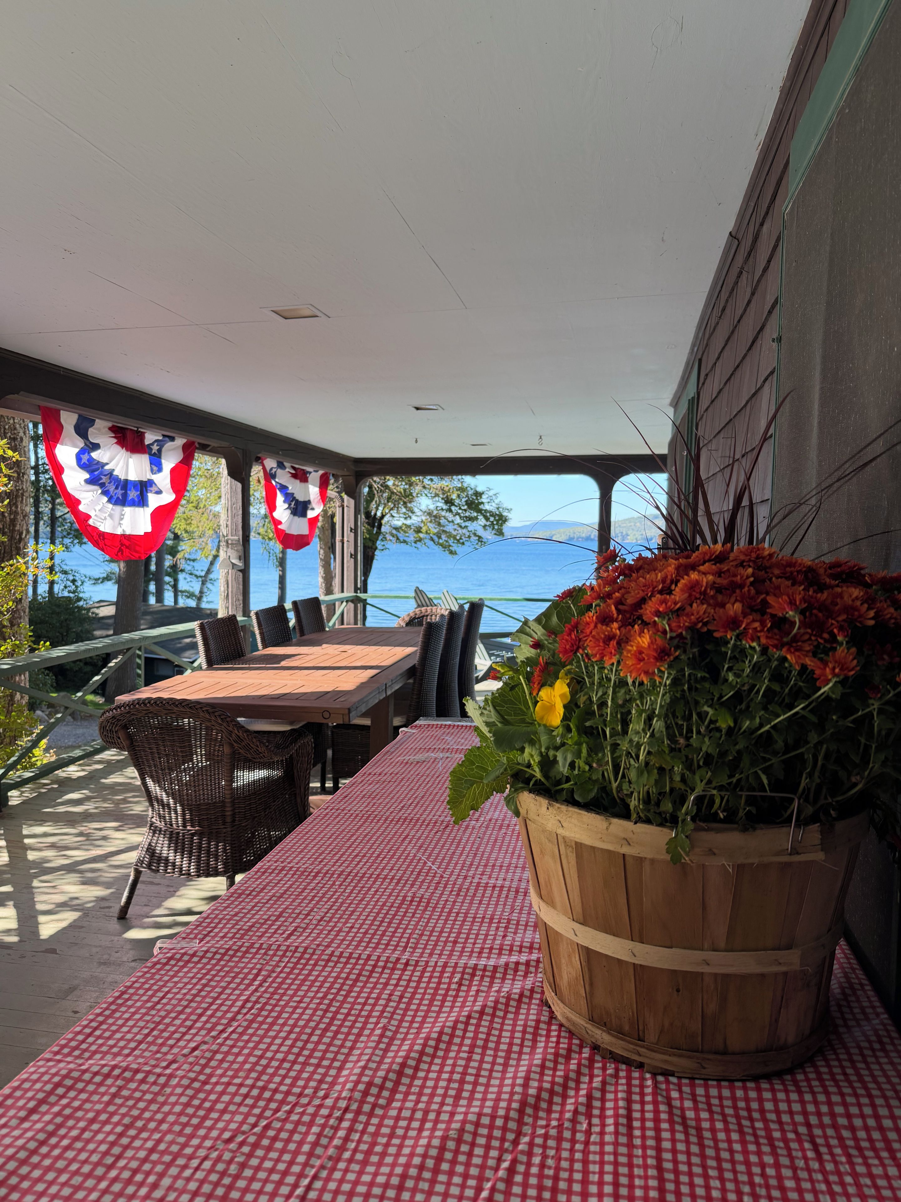 Une terrasse extérieure avec une table et des chaises, un jardinier en bois orné de fleurs et une vue sur l’eau.
