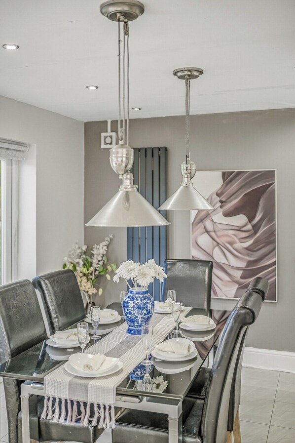 A dining area with a table set for four, two pendant lights, a vase with flowers, and a painting on the wall.