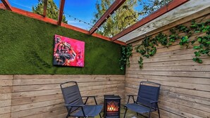 En udendørs patio med to stole, et lille bord og et bålsted.