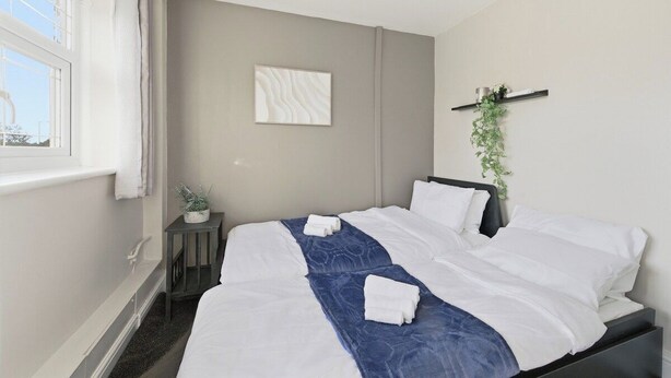 Et hotelværelse med en seng, et vindue, et natbord med en plante og et billede hængt på væggen.