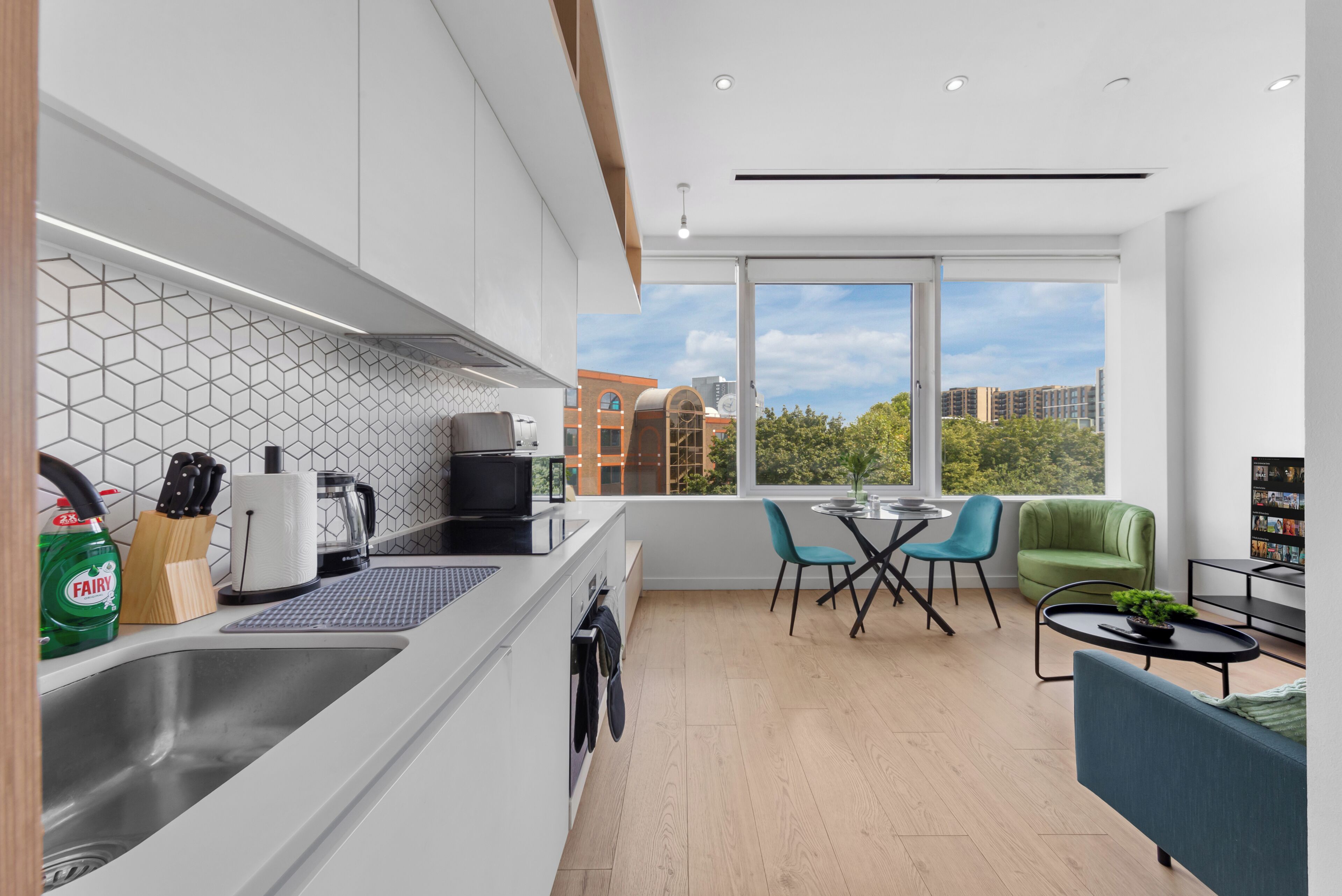 A modern kitchen with a large window, a dining area with a table and chairs, and a view of buildings outside.
