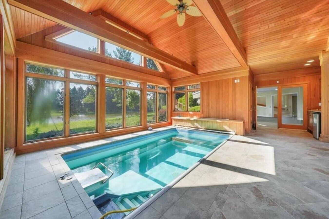 A large indoor swimming pool with a view of a green landscape through large windows.