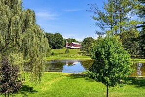 Eine friedliche Landschaft mit Teich, einem roten Bauernhaus und üppigem Grün.