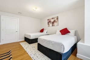 Ein Hotelzimmer mit zwei Betten, einer weißen Tür, einer Deckenleuchte und einem Bild an der Wand.