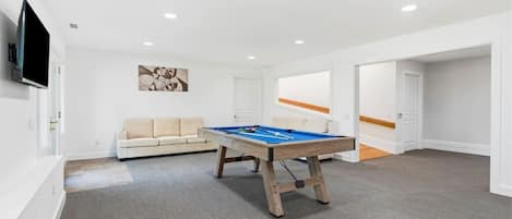 Una habitación con mesa de billar, un sofá y una televisión.