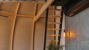 A modern interior with a curved ceiling, a green sofa, a wooden table, and a ladder.