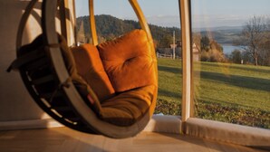 A room with a hanging chair by a large window overlooking a landscape.