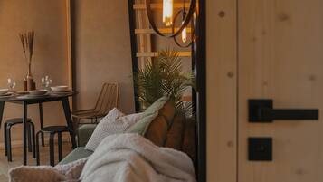 A cozy room with a bed, a table with glasses and bowls, a chair, and a hanging light fixture.