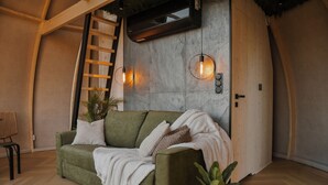 A cozy interior with a green sofa, a ladder, a wall-mounted air conditioner, and a potted plant.