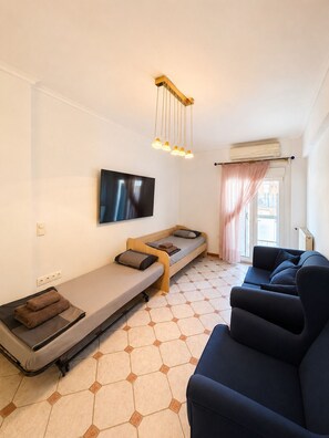 A modern living room with a sofa, a long sleeper sofa, a flat-screen TV, and a ceiling-mounted light fixture. -  2-bedroom apartment with AC in Thessaloniki (Thessaloniki)