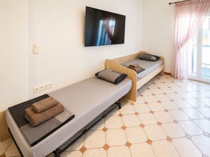 A room with two single beds, a flat-screen TV mounted on the wall, and a window with sheer curtains. -  2-bedroom apartment with AC in Thessaloniki (Thessaloniki)